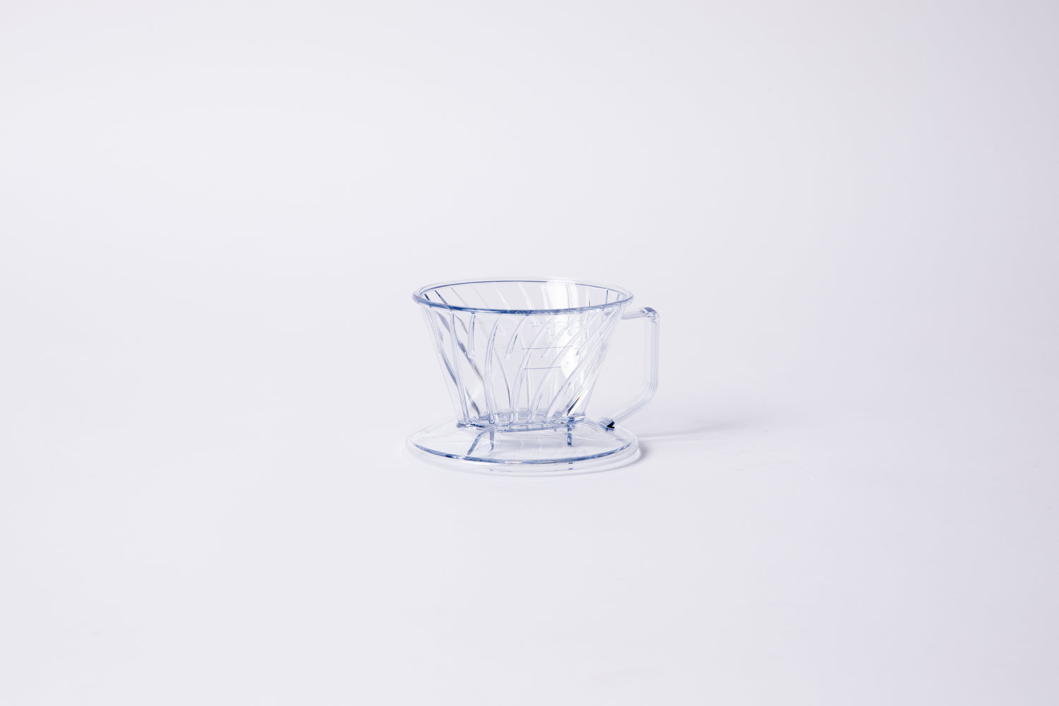 Clear plastic ribbed cone shaped dripper with a flat bottom base and handle. Set on a light gray background