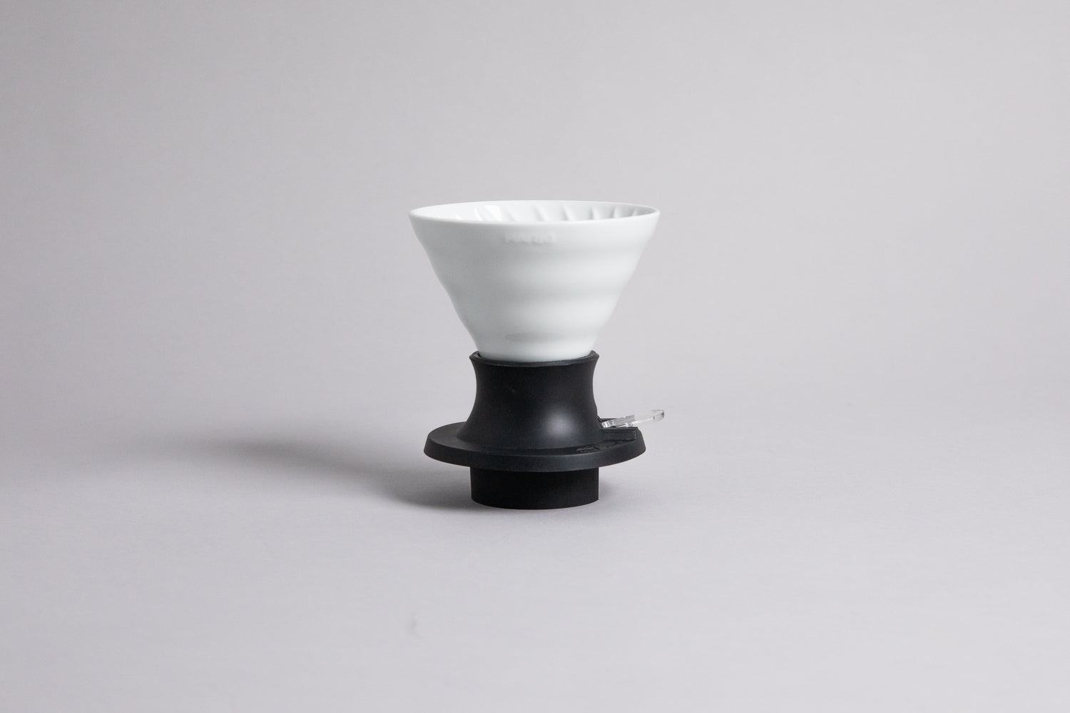 Cone-shaped white ceramic dripper seated in a black plastic silicone base with clear plastic push switch on a gray background.