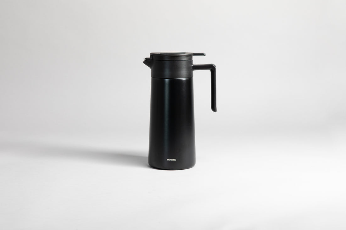 Black cylincial pot with an black polypropylene spout, handle and lid. Set on a light gray background