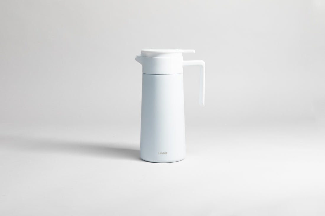 White cylincial pot with an white polypropylene spout, handle and lid. Set on a light gray background