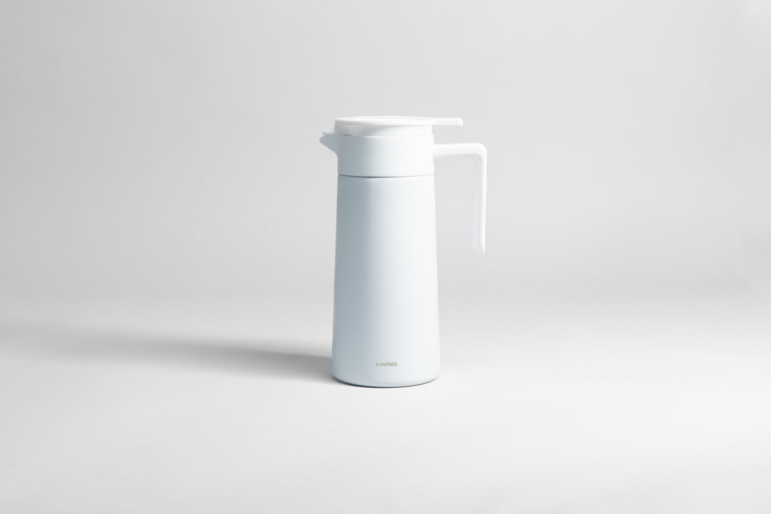 White cylincial pot with an white polypropylene spout, handle and lid. Set on a light gray background