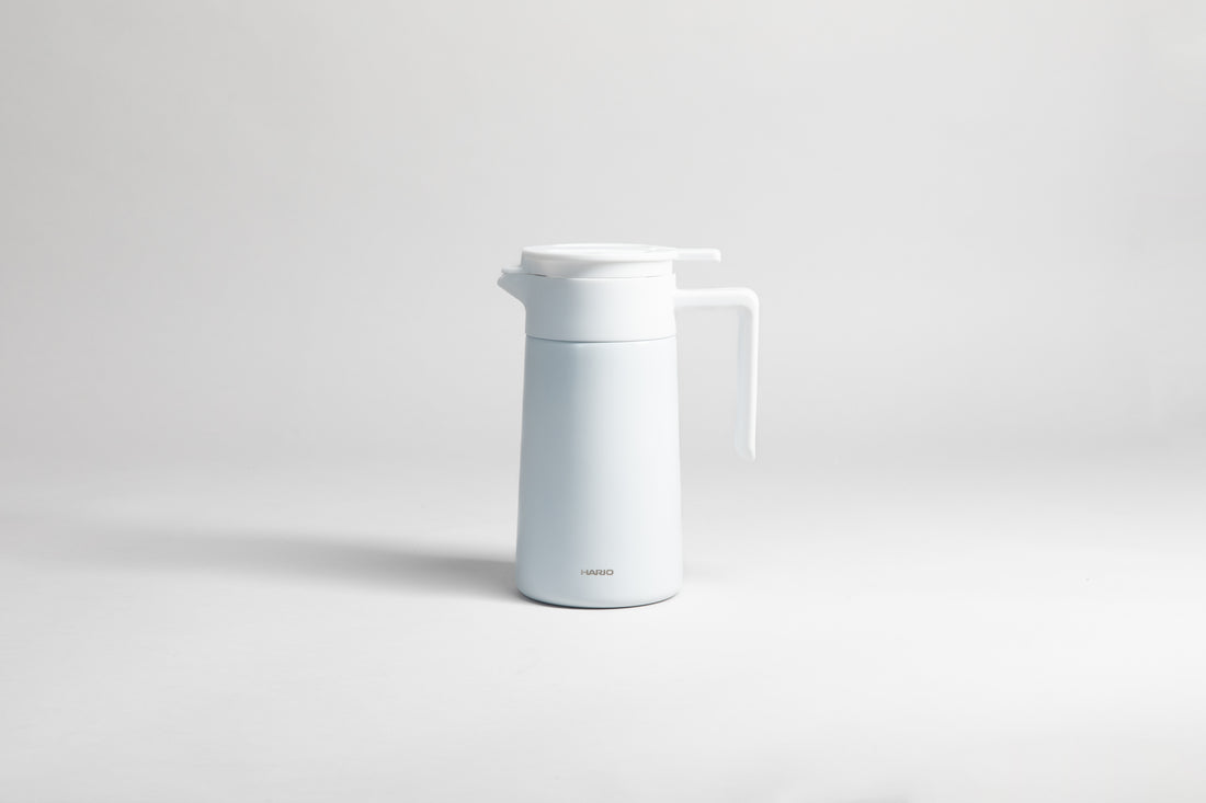 White cylincial pot with an white polypropylene spout, handle and lid. Set on a light gray background.