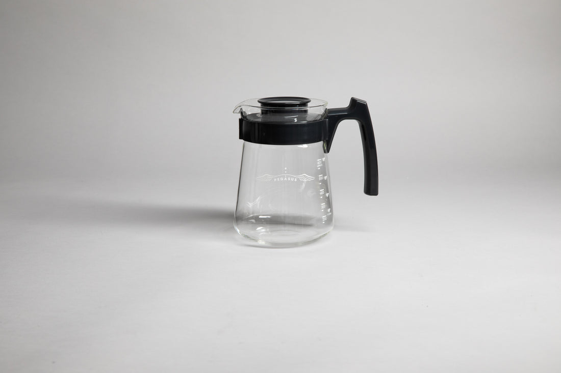 Glass coffee server with white text and level markings with black hard plastic handle and lid on a light grey background.