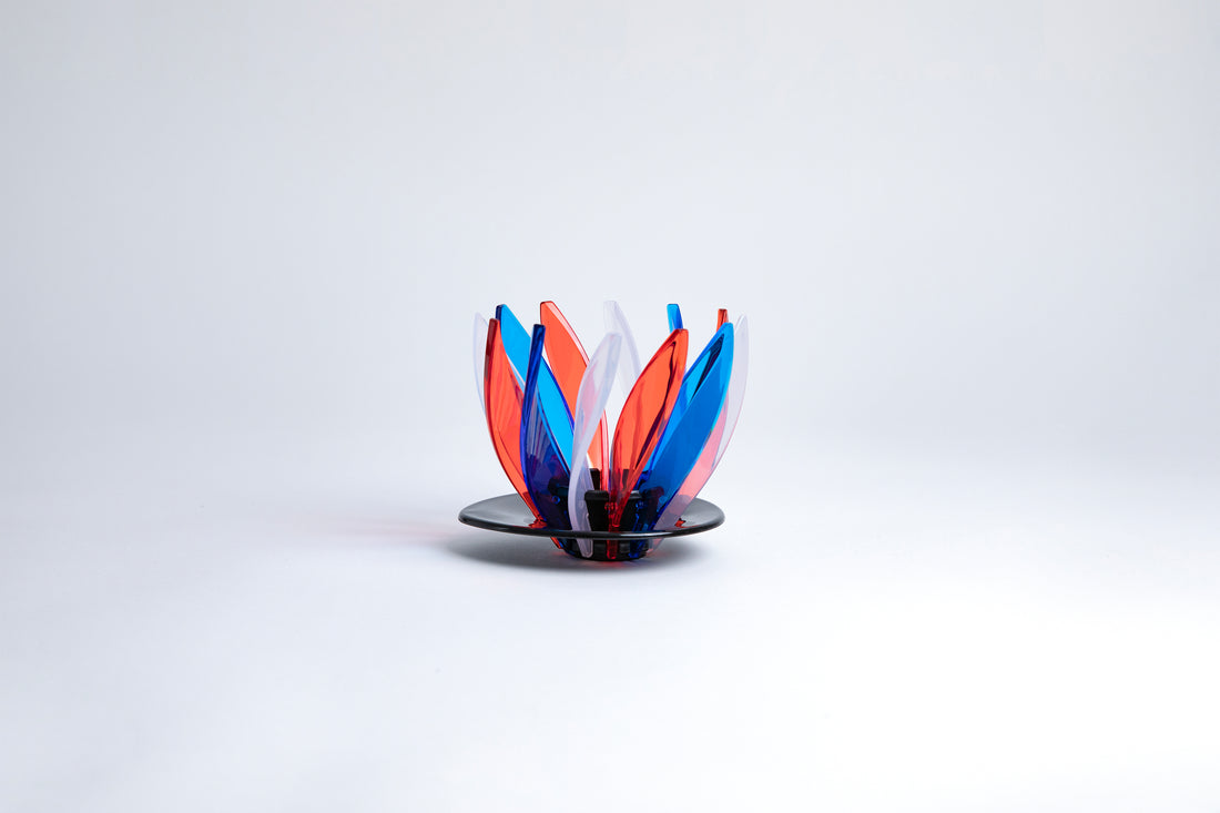 Transparent red, blue and clear pedals in a spiral shape on a transparent black base on a white background.