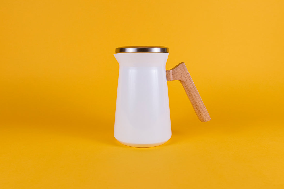 White stainless steel thermal serving carafe with wood handle and stainless steel lid set against a yellow background.